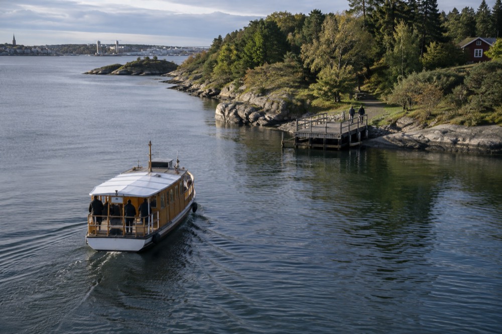 Small wooden ferry approaching a green island jetty on a calm fjord