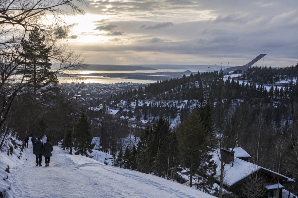 A ski jump tower on a hillside above a small town under a winter sky