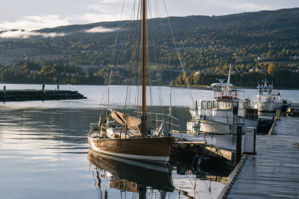 A wooden sailing boat and small ferries moored at a city pier on a calm morning