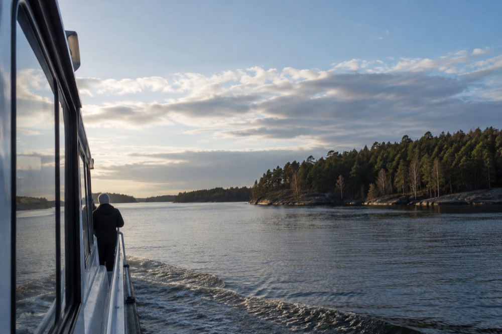 Electric passenger boat moving slowly past forested islands on calm water