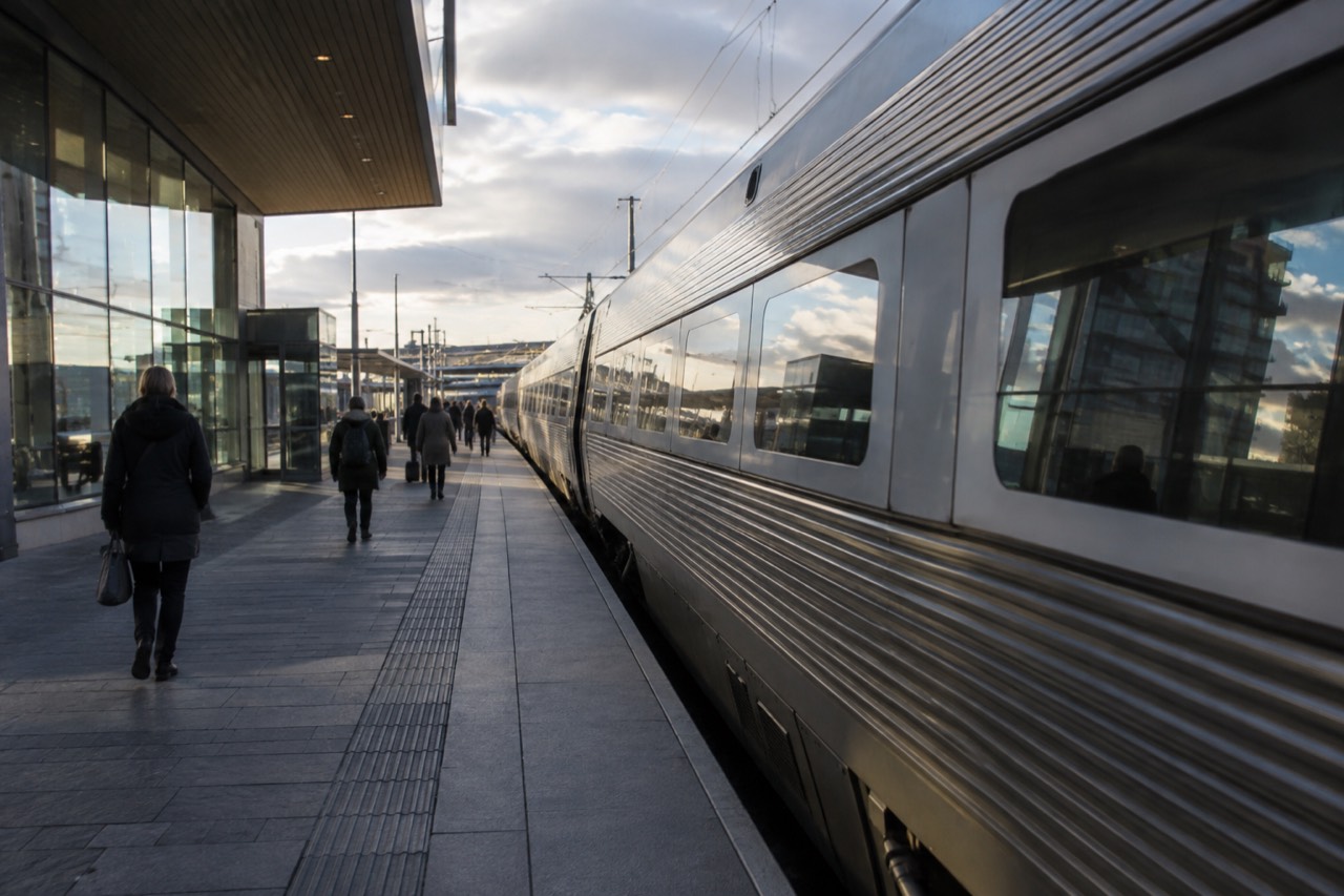A long-distance train waiting at a platform beside a modern Scandinavian station building