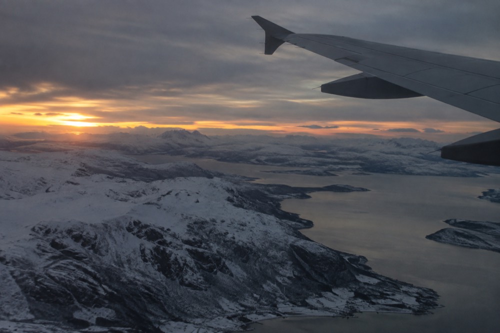 Aircraft wing above snow-covered Norwegian mountains at dusk