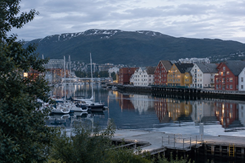 Tromso waterfront with wooden houses reflected in calm water on a bright summer night