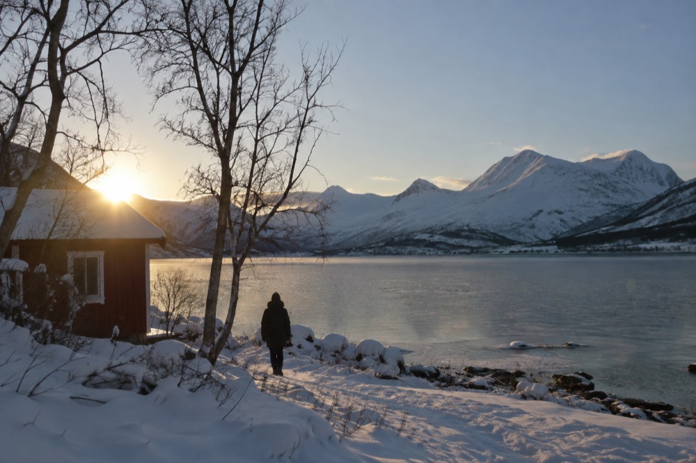 Small red wooden cabin under starry sky beside a frozen lake