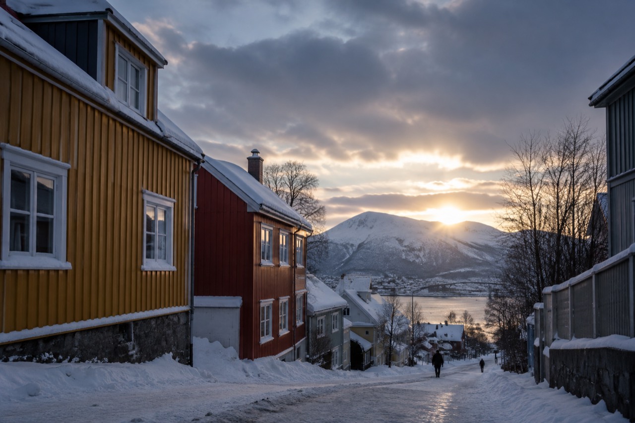 Snow-covered street with colorful wooden houses under a dark winter sky in northern Norway