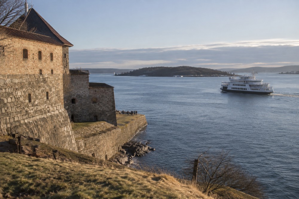 White cruise boat passing the stone walls of a waterfront fortress