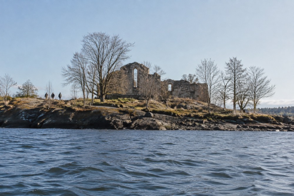 Ruined stone abbey walls on a small wooded island seen from the water