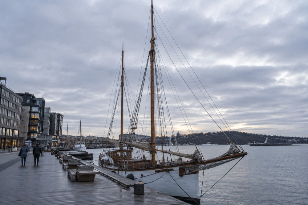 Wooden sailing ship with masts and furled sails moored at a city pier