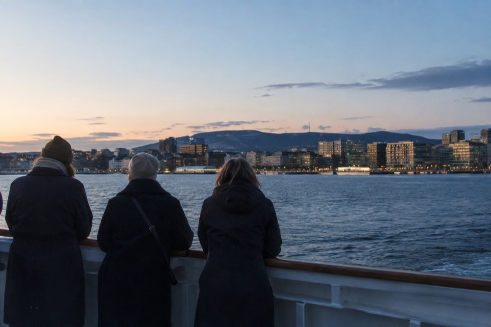 Passengers at the rail of a boat watching a city skyline recede across the water