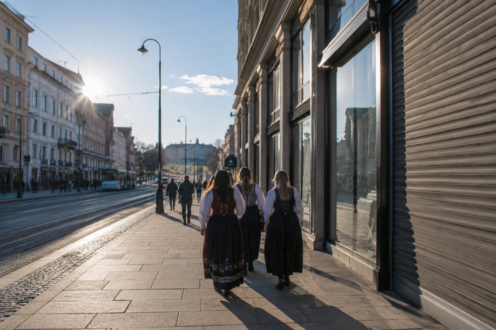 People in traditional folk dress walking beside a closed shopfront with Norwegian flags