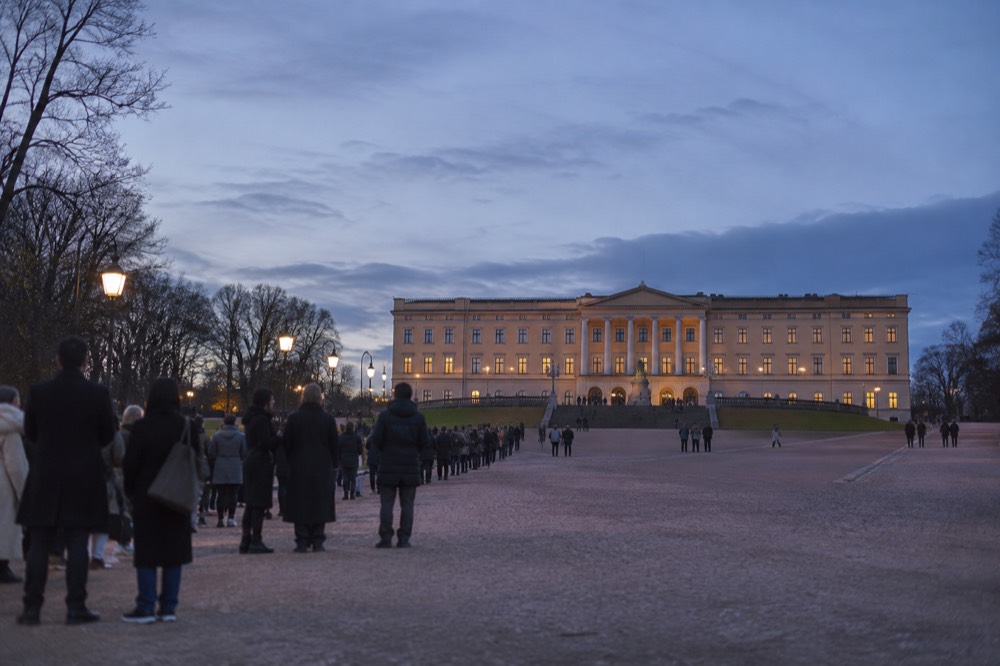 Spectators lining a boulevard in front of a large royal palace facade