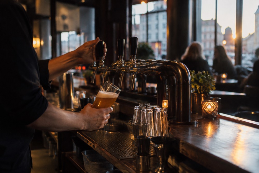A bartender pouring a beer behind a wooden counter in a dim Oslo bar