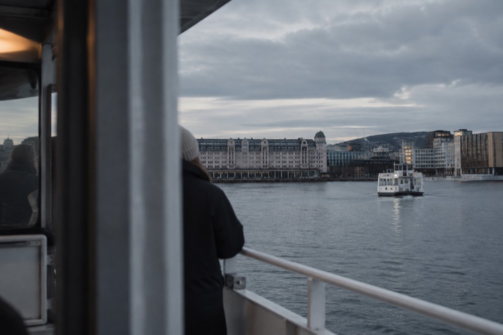 A boat on calm fjord water with Oslo buildings behind it