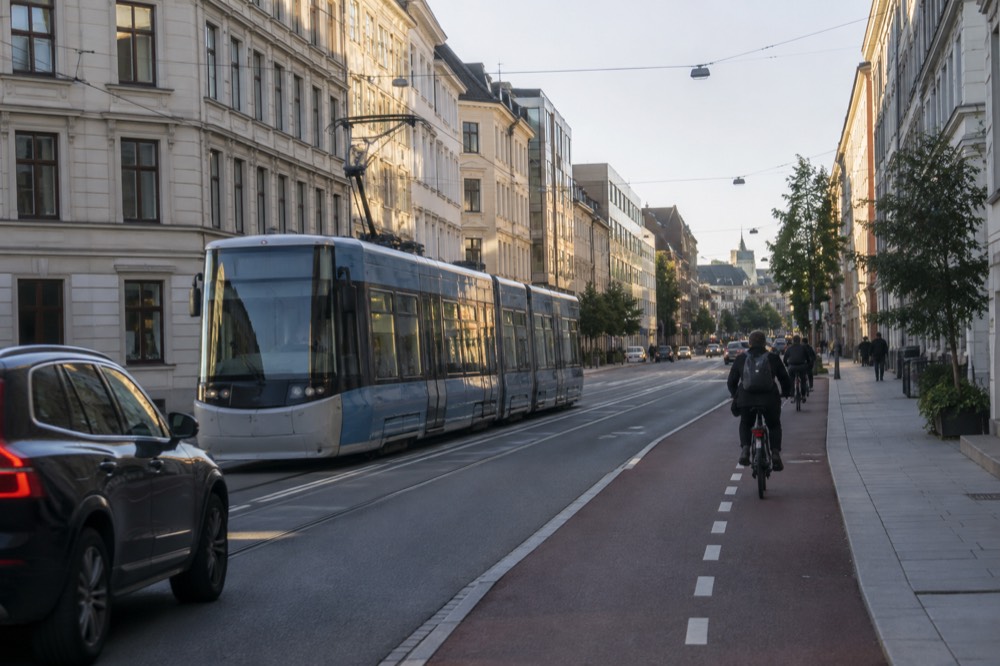A car driving on an Oslo street with a tram passing and cyclists in a bike lane