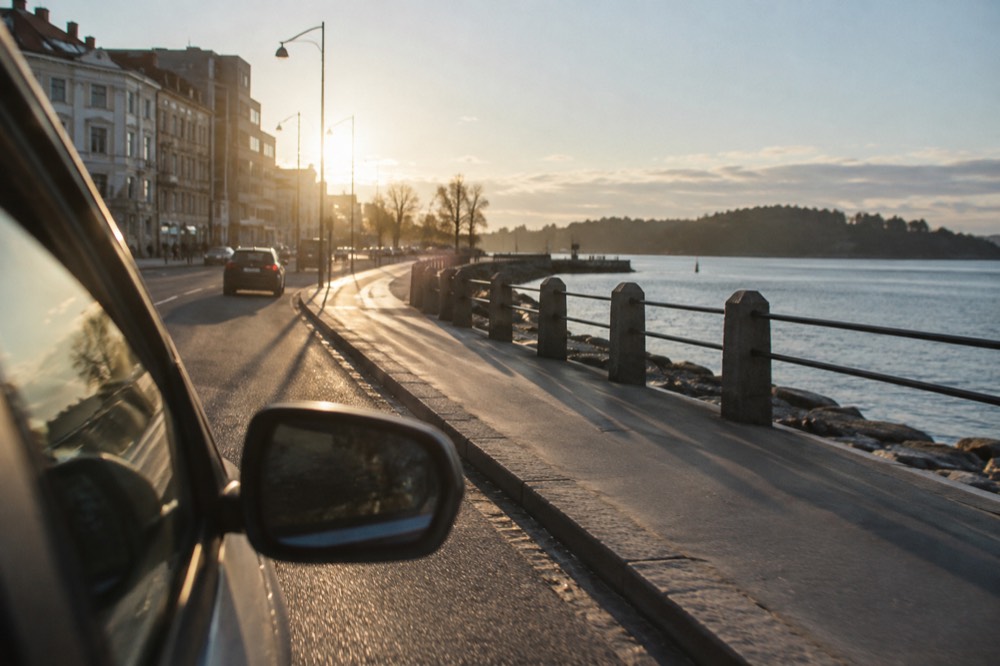 A car on a coastal road beside the Oslofjord with water and wooded shoreline