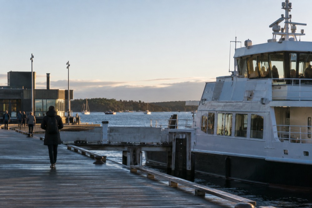 A ferry at a wooden Oslo pier with island shoreline and small boats beyond