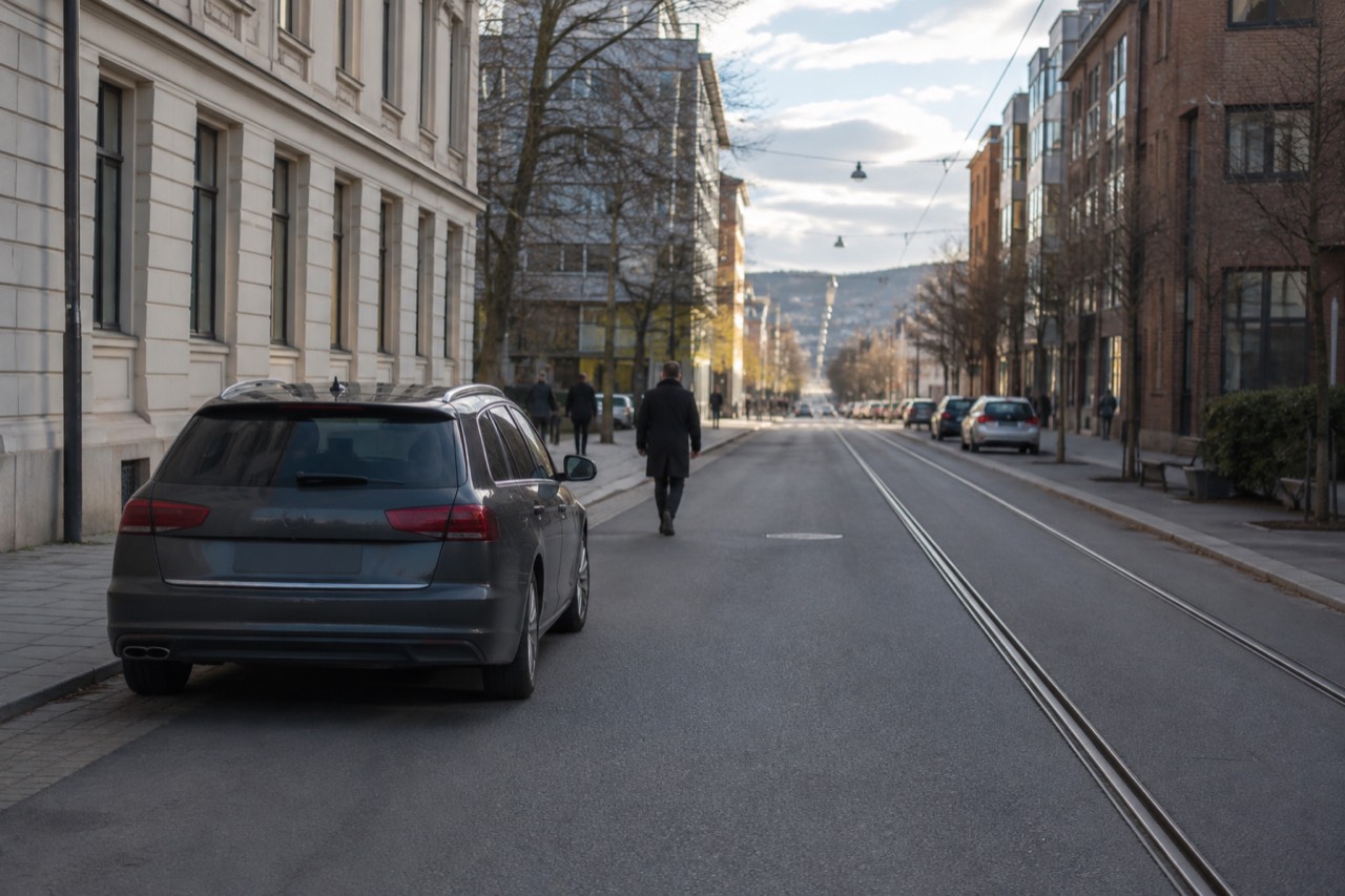 A rental car parked on a quiet Oslo street with tram lines and brick buildings