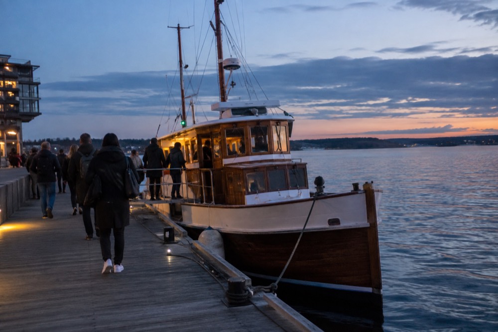 A wooden fjord boat moored at an Oslo pier with passengers boarding