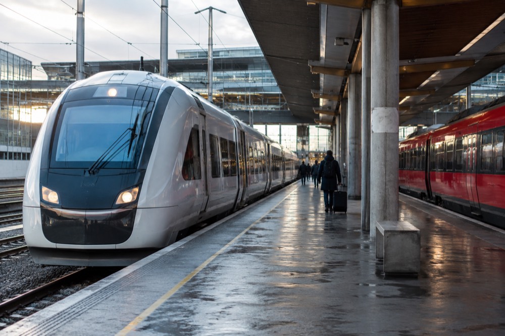 A sleek white airport express train at a platform beside a red regional train at Oslo Airport Gardermoen station