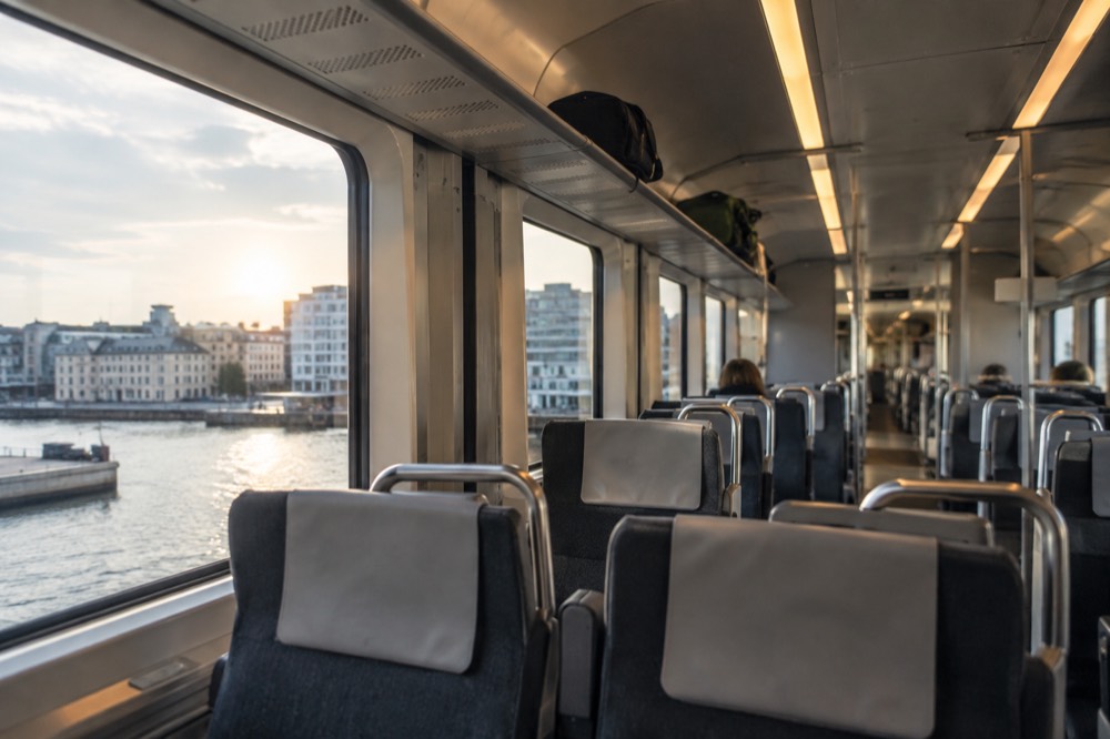 The interior of a modern airport train with rows of empty seats and luggage racks