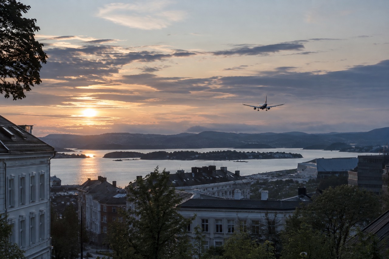 Airplane descending over a fjord landscape toward an airport runway at dusk
