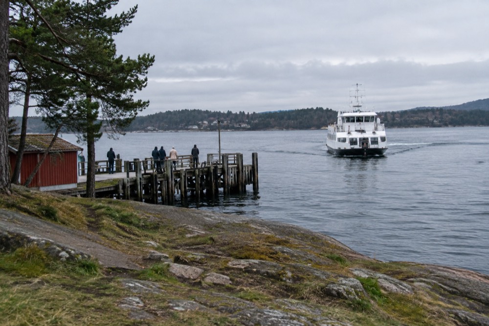 White passenger ferry approaching a wooden pier on a green Oslofjord island