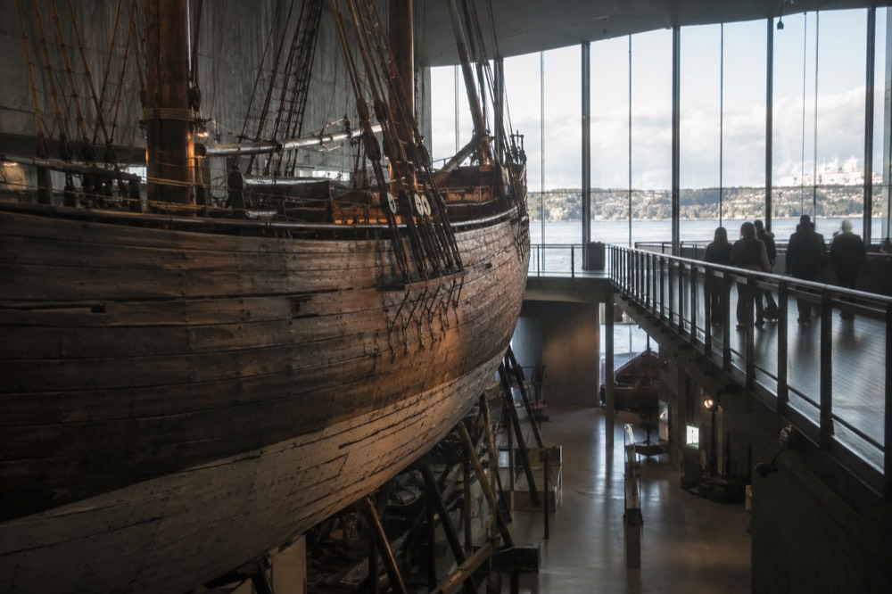 Wooden expedition ship hull inside a museum hall with visitors along a walkway
