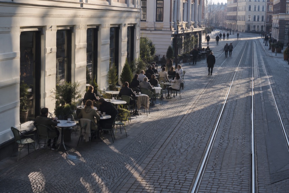 Outdoor cafe tables along a cobblestone street in Oslo with people seated