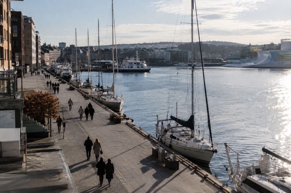 People strolling along a waterfront promenade with moored sailboats