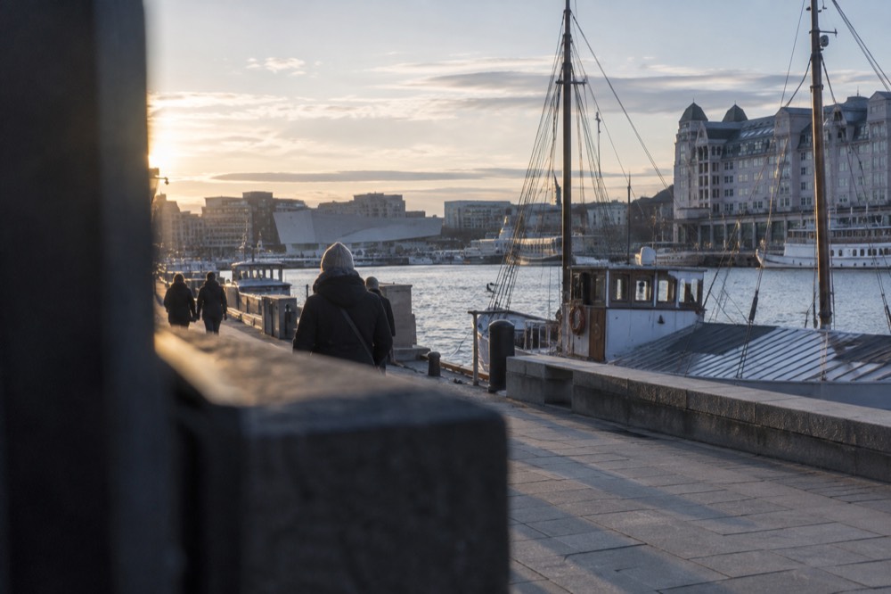 A waterfront promenade in Oslo with moored boats and museum buildings in the distance