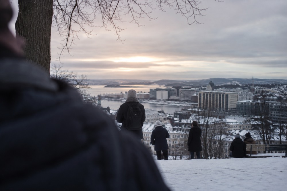 People gathered on a snowy hillside overlooking a city skyline at dusk