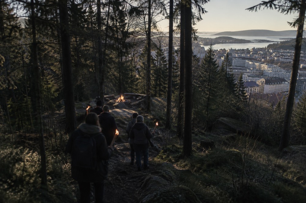 Group walking through dark forest carrying torches toward a glowing campfire