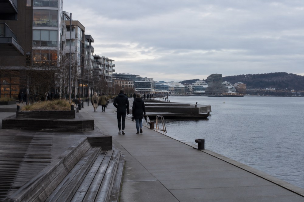 Flat modern waterfront promenade at Sørenga with people strolling beside the fjord