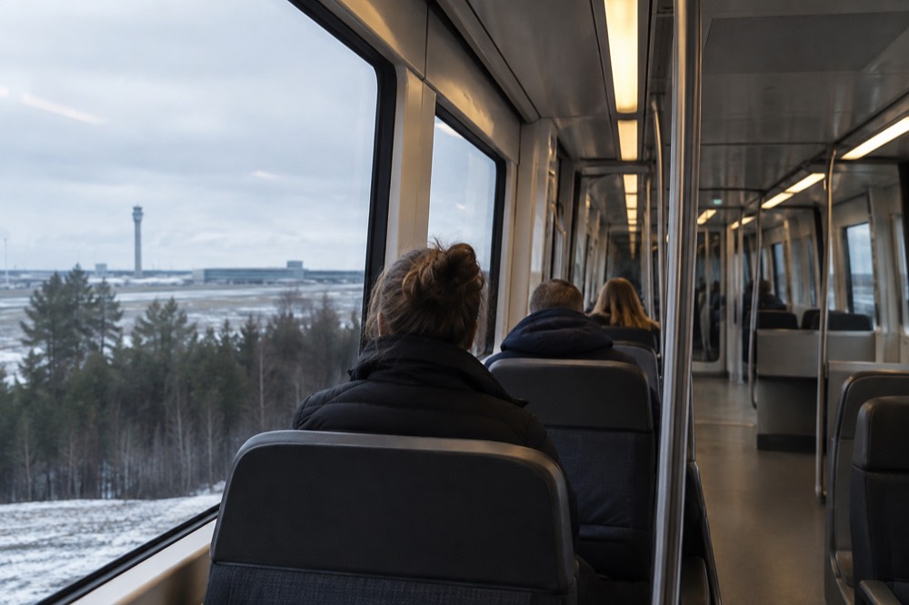 Interior of a modern airport train with passengers seated facing large windows