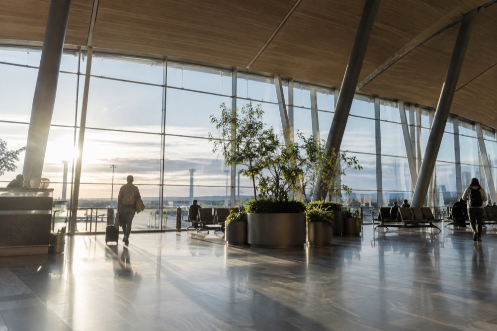 Spacious airport concourse with glass walls, wooden ceiling details and signage