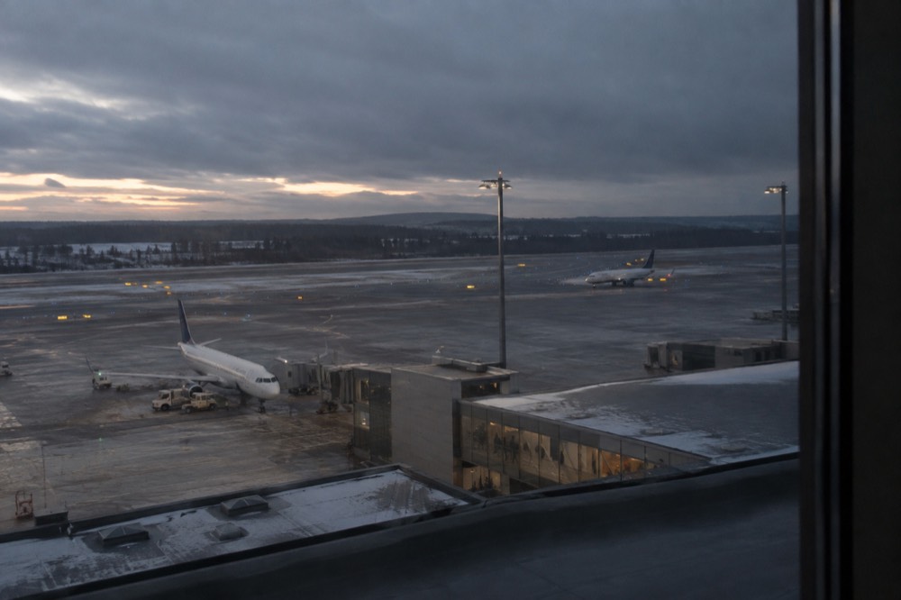 Hotel room window overlooking a runway at dusk with aircraft lights
