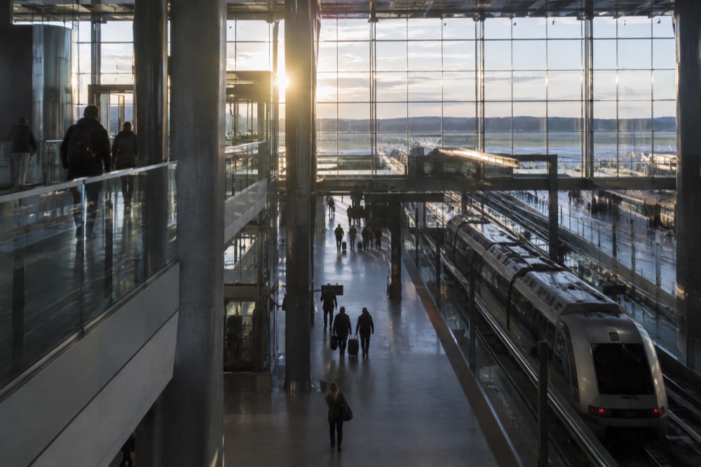 Modern airport terminal interior with train platform signs and travellers with luggage