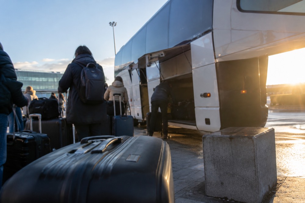 Airport coach parked at an outdoor bus bay with passengers loading luggage