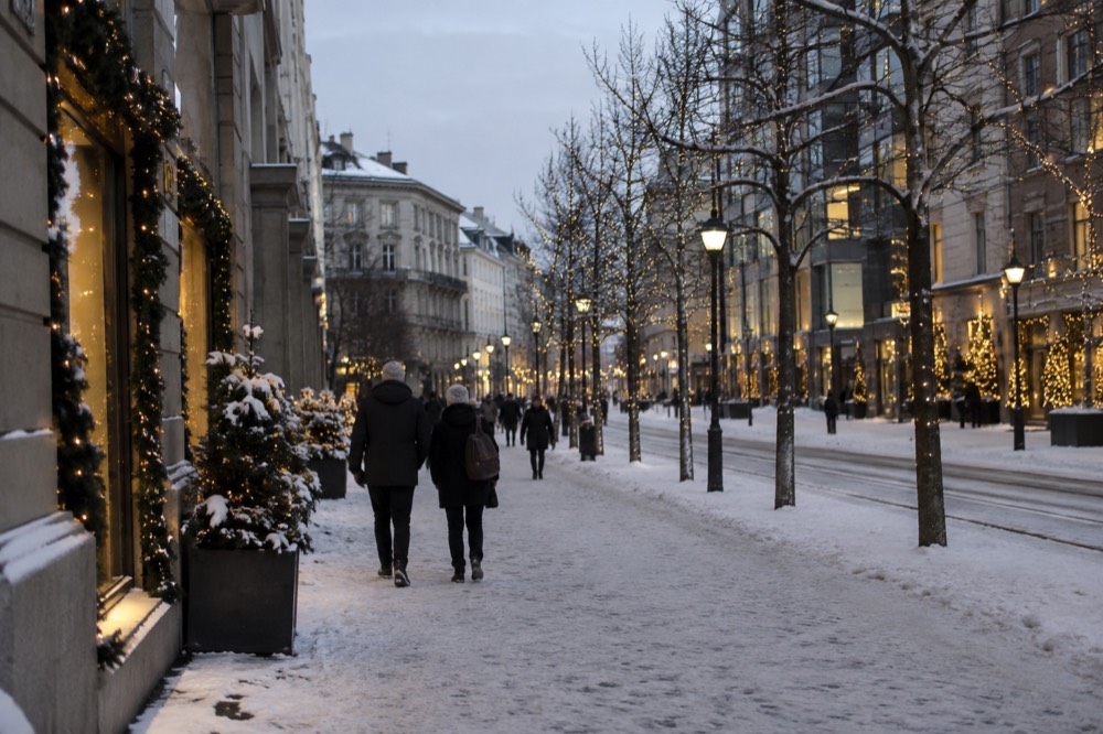Illuminated Christmas trees and decorated storefronts along a snowy pedestrian street at dusk