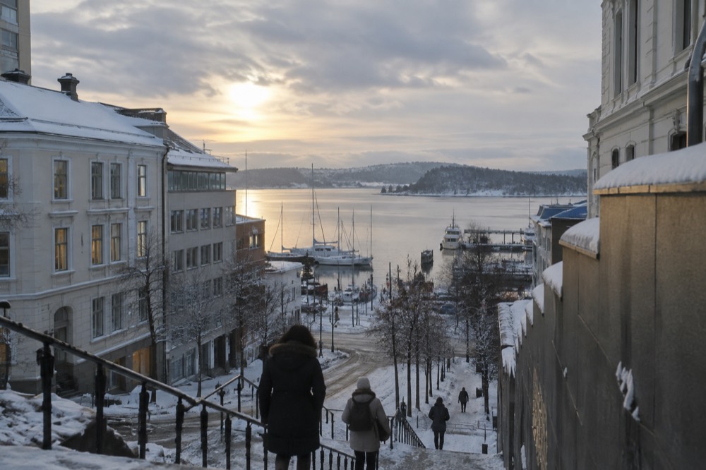 Low winter sun over a snow-dusted fjord with moored boats and a distant forested shoreline