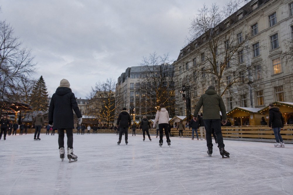 Skaters circling an outdoor ice rink surrounded by lit trees and wooden stalls