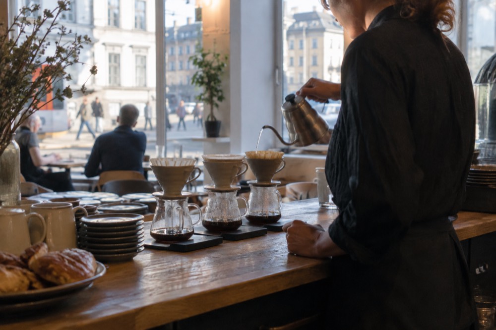 A barista pouring filter coffee behind a wooden cafe counter in Oslo