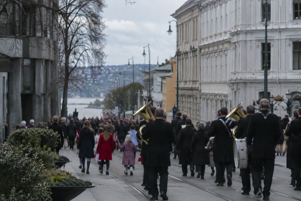 A brass band and children with flags marching in a parade past civic buildings in Oslo