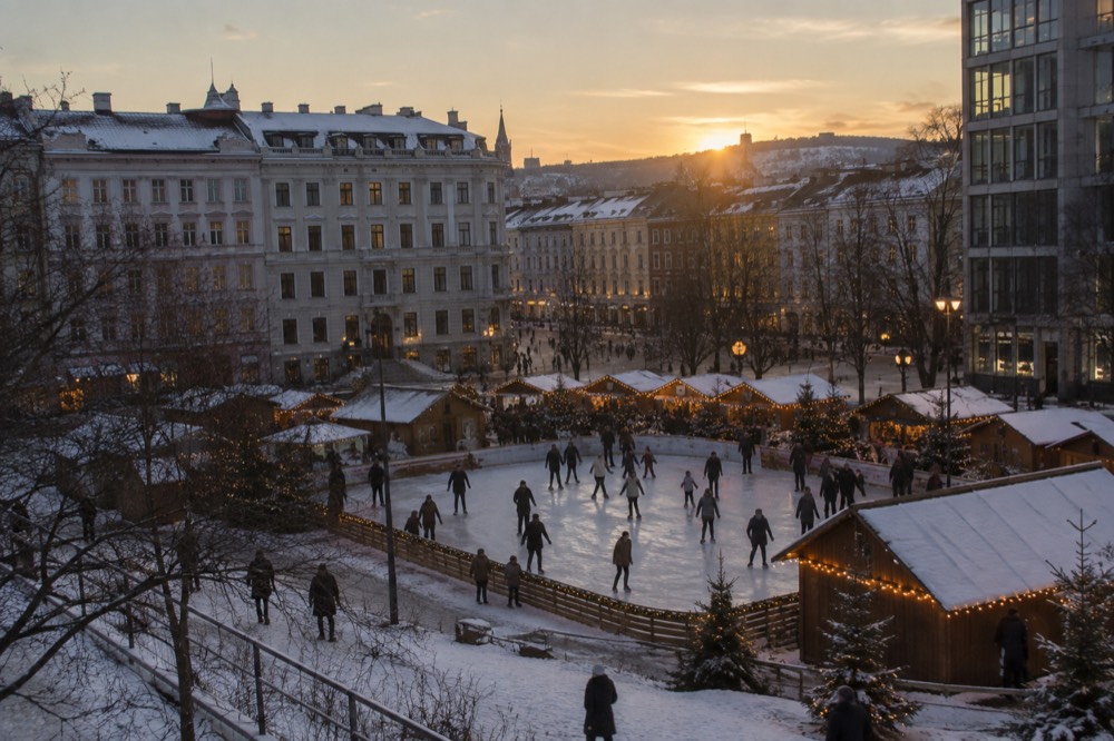 An outdoor ice rink surrounded by lit market stalls on a winter evening in Oslo