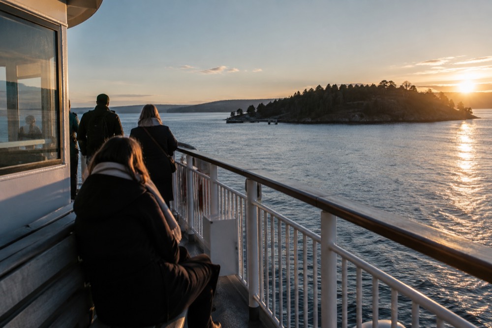 A passenger ferry moving across calm fjord water toward an island in the Oslofjord