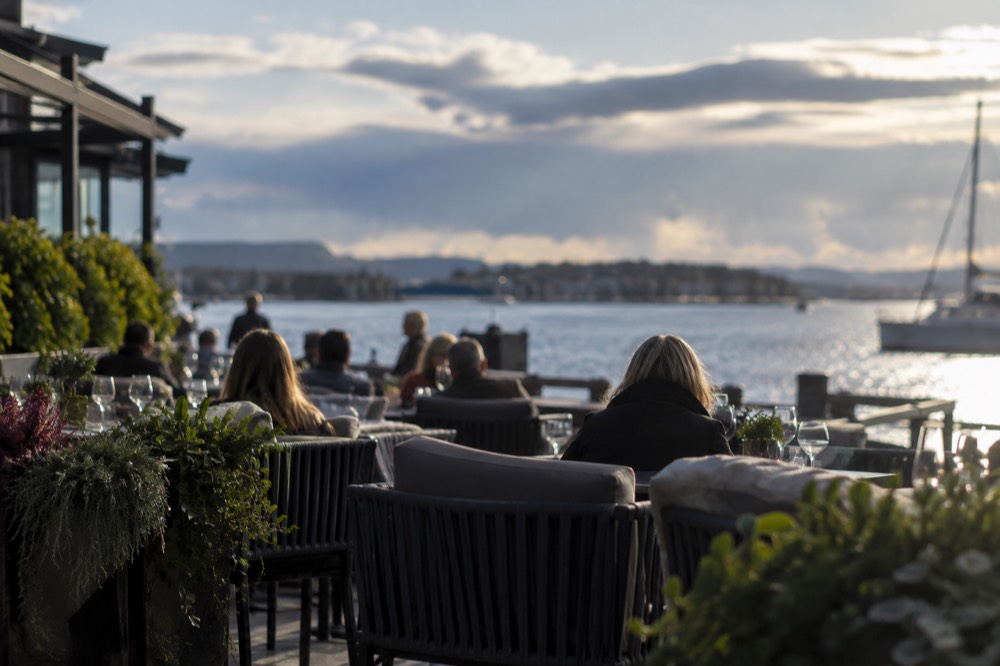 People sitting outside a waterfront restaurant in evening light at Aker Brygge in Oslo