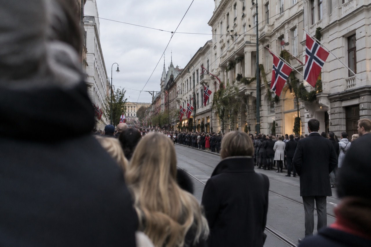 Crowds gathered along a city street in Oslo with Norwegian flags and decorated buildings