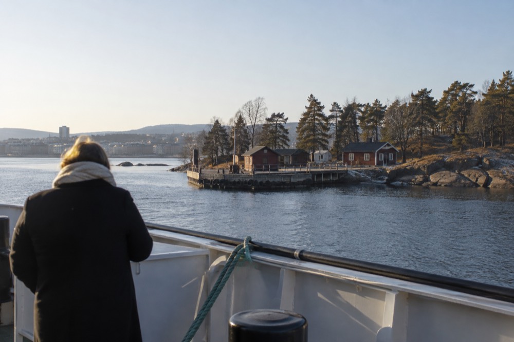 A public ferry approaching a small island dock with wooden cabins among pine trees