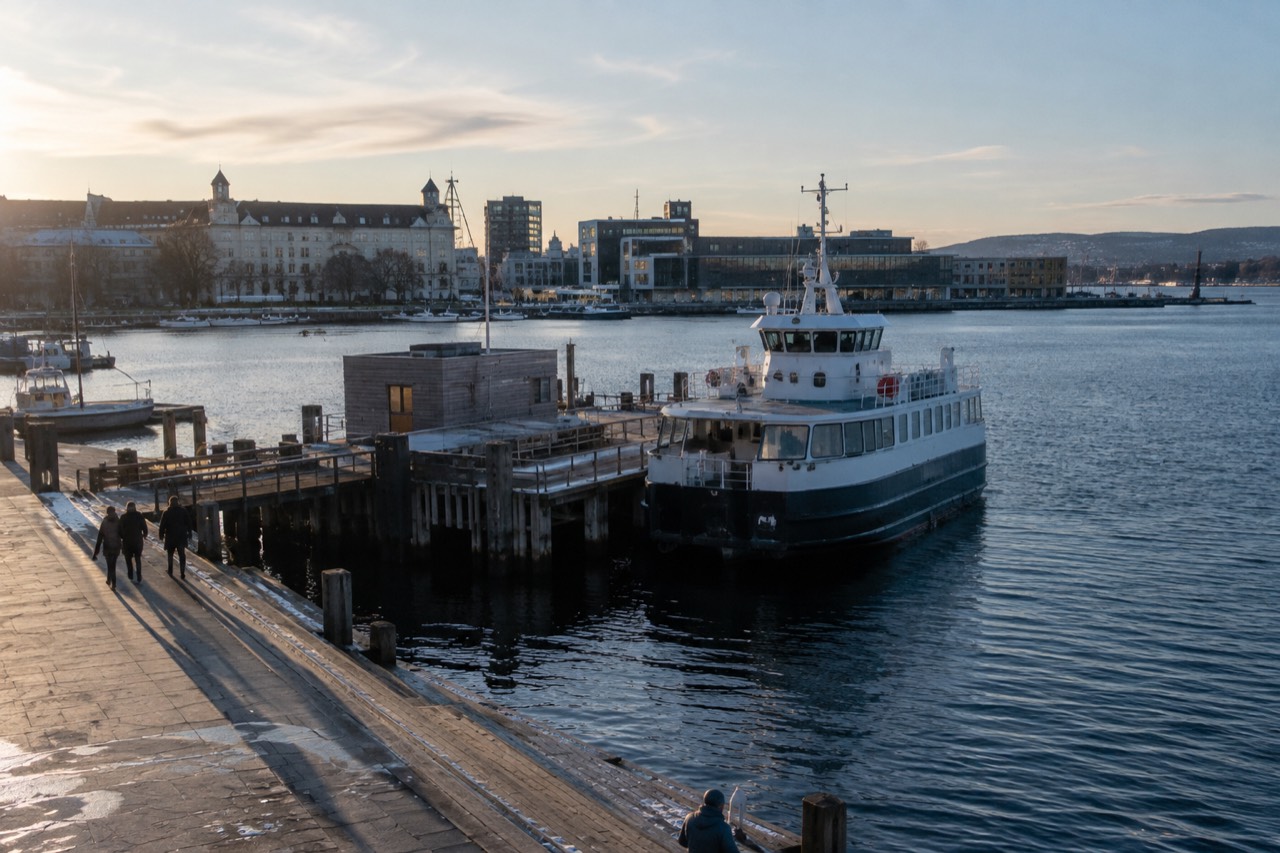 A passenger ferry moored at a wooden pier on the Oslofjord with museum buildings behind