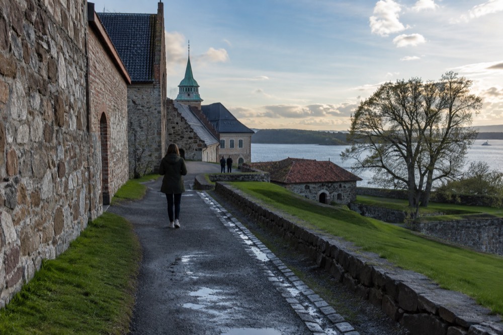 Medieval stone fortress walls with green grass and fjord water beyond